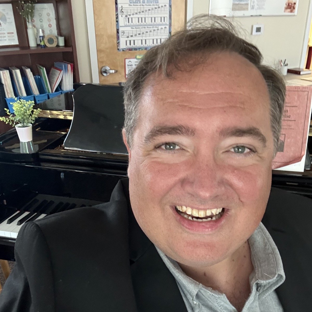 R.J. Nestor smiling in a black jacket, a grand piano behind him